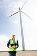 Engineer Inspecting Wind Turbine Efficiency in Vast Green Field on a Sunny Day.