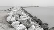   A black-and-white image of rocks and a lighthouse in the distance during a foggy, overcast day
