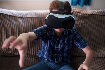 Young kid immerse within the Virtual reality world wearing VR headset gaming and entertainment having fun. At home living room online internet device technology concept.