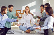 Calm, tranquil woman sitting on office table in lotus yoga pose, mediating, chilling out, and ignoring team of diverse colleagues who are demanding to do lots of work as soon as possible