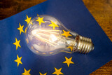 Fototapeta  - A glowing light bulb lying in the middle of the European Union flag, Concept, Energy prices in EU countries, Changes resulting from energy policy