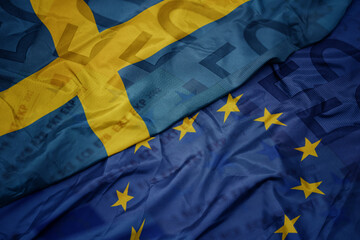 waving colorful flag of european union and national flag of sweden on a euro money banknotes background. finance concept.