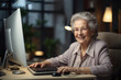 An old woman is sitting at a computer. Smiling.He communicates via the Internet.