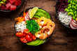 Balanced diet poke bowls with tuna, salmon, shrimp, vegetables, legumes, avocado and rice, wood table background, top view
