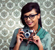Glasses, photography and portrait of woman with camera and funky, trendy and cool fashion for job. Smile, photographer and female person with casual outfit and vintage dslr equipment by wallpaper