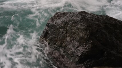 Poster - A large rock is in the ocean with waves crashing around it. The water is a deep blue color and the rock is a dark grey color. Scene is calm and peaceful, as the rock stands strong against the waves