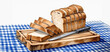 A loaf of bread, partially sliced, rests on a cutting board with a knife, atop a blue checkered cloth