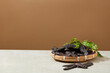 A rattan tray with many black locust fruit above placed on the left side of white table over brown background. Photo was taken from front view with space for text and displaying product