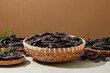 A round bamboo basket within black locust fruit placed in center of photo, surrounded by some bamboo tray against on brown background. Space for displaying product, front view