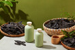 Photo with view from above, a few bottle without label placed on light gray table decorated by black locust fruits in bamboo baskets. Mock up for advertising with moss green background