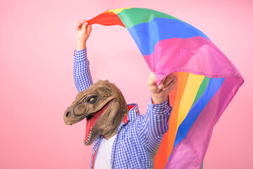 man with T rex head waves a rainbow flag on an isolated pink background. surreal and fun concept