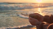 The Close Up Picture Of The Person Is Holding The Cup Of The Coffee By Their Own Hand Also Walking At The Side Of The Beach Near The Sea Or An Ocean That Has Been Shine By The Light From A Sun. AIG43.