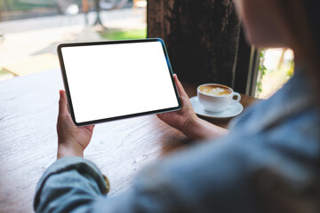 Mockup image of a woman holding digital tablet with blank white desktop screen in cafe