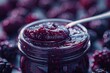 Blackberry jam. Spoon scooping homemade blackberry jam from a glass jar surrounded by fresh blackberries.
