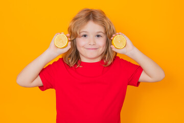 Wall Mural - Kids face with fruits. Child hold lemon in studio. Studio portrait of cute kid boy with lemon isolated on yellow.