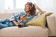 Happy woman relaxing at home, reading on tablet PC, listening to music with headphones on couch