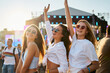 © artiemedvedev - Group of joyful girls at beach music festival. Friends dance, celebrate summer event, arms raised. Bright sunlight on smiling faces. Youth joy, live concert fun. Casual fashion, friendship moments.