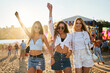 © artiemedvedev - Group of cheerful young women dancing at beach music festival, sunset flares. Friends in summer outfits, sunglasses enjoy concert. Carefree girls celebrate, fun on sandy shore at fest event.
