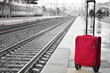 a red suitcase near the tracks at the train station
