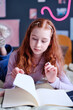 Vertical medium closeup of modern teen girl looking through notes in notebook while working on school project at home