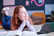Portrait of modern teen girl with curly read hair daydreaming while doing homework in her bedroom, copy space