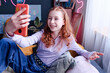 Cheerful teen girl holding smartphone sitting on her bed chatting on video call, high angle view