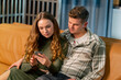 © Guys Who Shoot - young couple in love on yellow sofa hugging and flirting reading the news on the phone