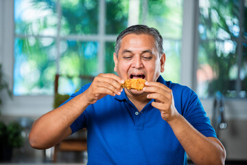 Indian asian mid age handsome man eating chicken leg piece with happiness