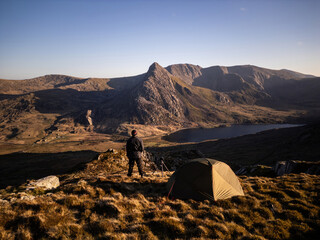 Wall Mural - An explorer and photographer on a mountain summit overlooking a spectacular valley from his wild camping tent