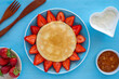 Pancakes and strawberries laid out in the form of flower on blue background.