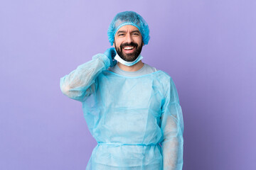 Wall Mural - Surgeon man with beard with blue uniform over isolated purple background laughing
