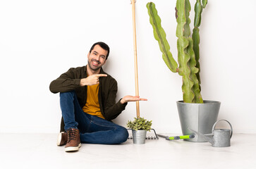 Wall Mural - Gardener man sitting on the floor at indoors holding copyspace imaginary on the palm to insert an ad