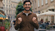 Happy smiling enthusiastic Indian Arabian ethnic male man guy businessman looking at camera positive winner rejoice victory celebrating win luck triumph showing thumbs up gesture outdoors city street