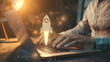 © Théo - A businessman working on a laptop with a virtual screen showing a rocket icon and up arrow, indicating fast startup business and strategic planning for success.
