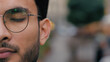 Close up young confident professional Indian Arabian ethnic guy male student model businessman man's face eye glasses eyewear looking at camera outside blurred background. Healthy entrepreneur smiling