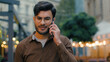 Successful confident happy Indian Arabian ethnic man male student guy businessman talking mobile phone cellphone conversation speaking communication business call connection outdoors city urban street