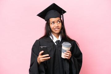 Wall Mural - Young university Colombian woman graduate isolated on pink background holding coffee to take away and a mobile while thinking something