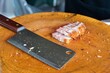 A knife is on a wooden cutting board with a piece of meat on it. The knife is sharp and has a black handle. The meat is sliced into thin pieces