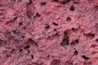 A wall with a red and pink texture. The wall has many holes and is rough to the touch