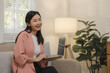 A beautiful Asian woman is using a communication device to talk to long-distance friends abroad, Relax on the couch at home and do your own recreational activities.