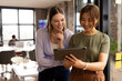 © Wavebreak Media - A mature Asian female professional and young Caucasian female colleague holding a tablet in a modern