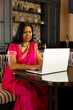 © Wavebreak Media - A middle-aged Indian woman wearing pink sari, using laptop at home
