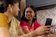 © Wavebreak Media - Indian mother and daughter, smiling at home, looking at smartphone