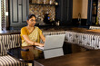 © Wavebreak Media - Indian young woman wearing yellow top and sari, working on laptop at home