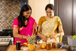 © Wavebreak Media - Indian mother and teenage daughter in traditional sarees preparing food at home