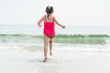 Young Girl in Pink Bathing Suit Running into Beach Waves