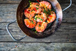 Fried prawns with thyme in cooking pan on wooden table
