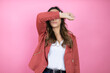 Young beautiful woman wearing casual jacket over isolated pink background covering eyes with arm smiling cheerful and funny. Blind concept.