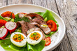 Tasty salad - roasted beef loin boiled eggs and fresh vegetables on wooden table

