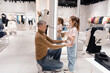 Father Helping Daughter Try on Clothes in a Bright Clothing Store During Shopping Day
